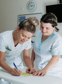 Binôme infirmière et aide-soignante souriantes discutant avec un patient