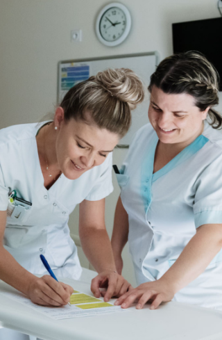 Binôme infirmière et aide-soignante souriantes discutant avec un patient